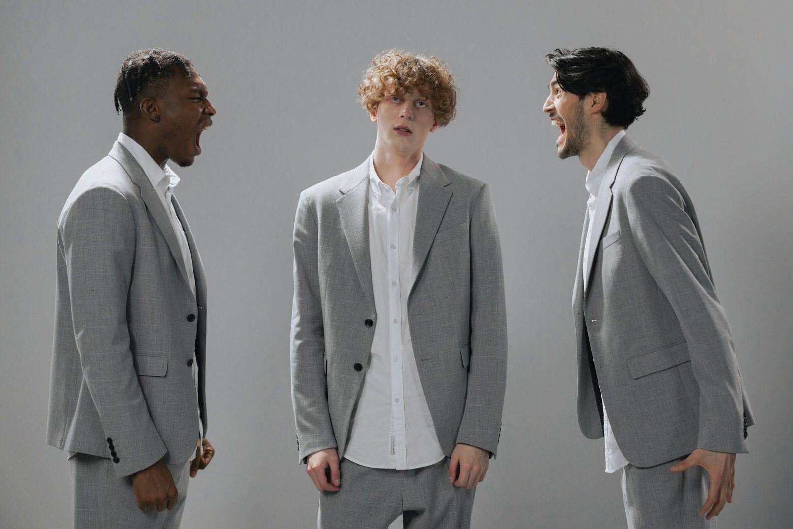 Three businessmen in gray suits arguing during a studio photoshoot with a gray background.